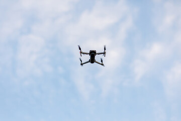 Drone flying on blue sky with white clouds background. Bottom view Quadcopter with digital camera. Flying remote control Quadrocopter, UAV.