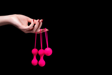 Woman's hand holds pink Kegel balls / Ben Wa balls on a black isolated background. Vaginal balls in a female hand. Sex toys Geisha balls. Place for text. Sex shop concept - obrazy, fototapety, plakaty