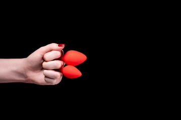 Two red anal plugs are clenched in a female hand into a fist on a black isolated background. Sex toys for ass. Copy space for text