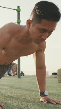 Young man doing push-ups on a sports ground by the sea