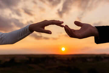 Hands of bride and groom reaching each other, touching fingers on sunset sky countryside background. Helping hands for save and support people concept. Wedding day. Valentine day.