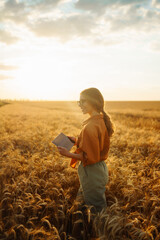 Young female farmer in her hands with a digital tablet in a wheat field checks the quality and...
