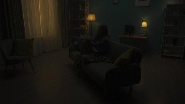 A devastated woman is sitting on a sofa in a dark room. A woman is desperately thinking about personal problems, going through a crisis, crying. Change of day and night. HDR BT2020 HLG Material.