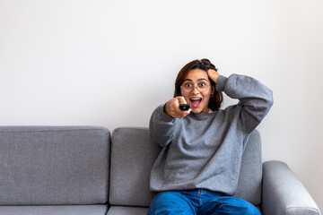 black-haired woman in gray sweatshirt watching tv surprised