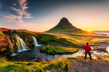 Sunrise over volcanic Kirkjufell mountain and photographer man standing in summer at...