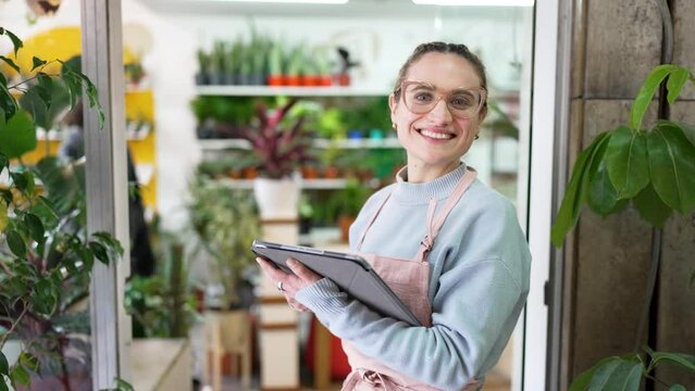 portrait beautiful smiling caucasian woman owner employee of a plant store business at the entrance with a tablet