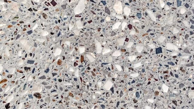 Background cement wall interspersed with multicolored rubble and marble chips, rotating, turning, close-up macro, top view
