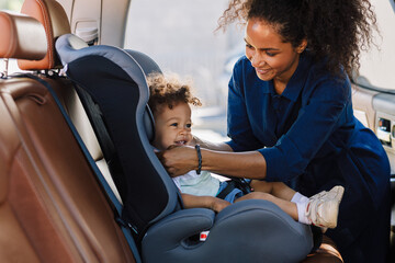 Happy mother adjusting belt on a baby car seat. Little boy smiling while his mother prepared his...