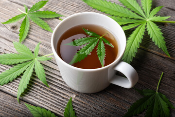 Tea with cannabis leaves on wooden table. Medical herbal tea with marijuana close up