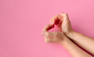 Women's hands in the shape of a heart on a pink background with space for text