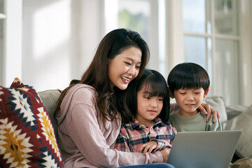 young asian mother and two children daughter and son sitting on family couch using laptop computer together at home