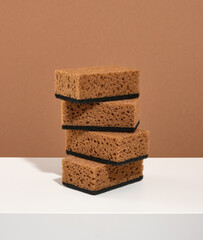 Brown dishwashing sponges lay one on top of the other on white table. Kitchen dish work.