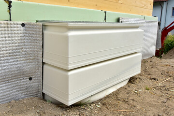 Lüftungsschacht mit Metallrost zur Lüftung des betonierten Kellergeschosses, montiert an einer mit Styrodur gedämmten und mit Noppenbahn abgedichteten Vollholz-Neubauhausfront