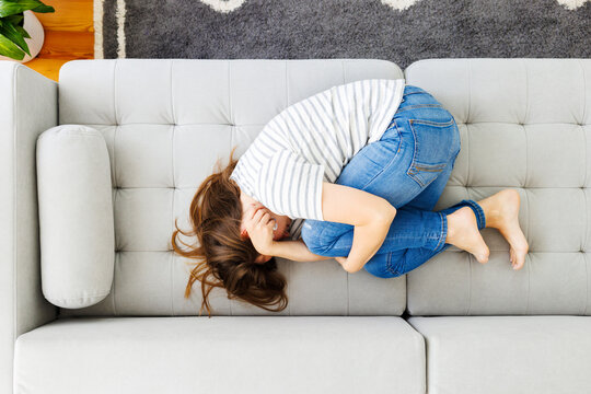 Frustrated woman covering face and crying, lying on sofa at home alone