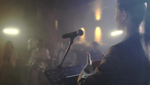 The performance of the girl in front of a small hall. An independent speaker speaks on stage in a conference room for young people. A woman explains motivation to a group of people.