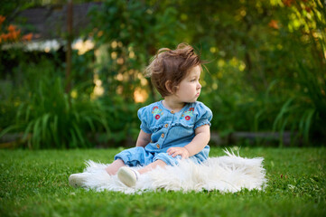 Adorable girl on the grass in the garden. Close up portrait. Happy little girl in summer scenery. Sweet small kid outdoors.