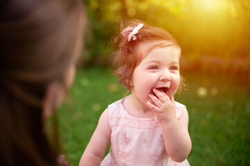 Adorable girl on the grass in the garden. Close up portrait. Happy little girl in summer scenery. Sweet small kid outdoors.