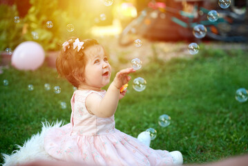 Adorable girl on the grass in the garden. Close up portrait. Happy little girl in summer scenery. Sweet small kid outdoors. A child plays with soap bubbles.