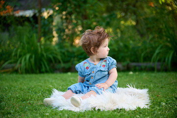 Adorable girl on the grass in the garden. Close up portrait. Happy little girl in summer scenery. Sweet small kid outdoors.
