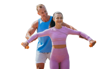Strong caucasian muscular fitness trainer assists to female client to make exercise with dumbbells against transparent background. Cheerful American couple training together. Fitness, sport.