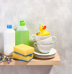 Set of clean tableware. Yellow dishwashing sponges, detergent dispensers. A yellow rubber duck sitting in a clean cup.