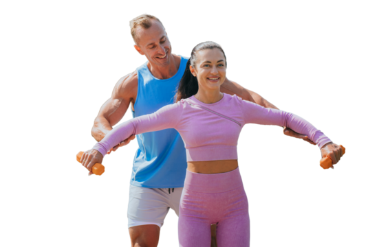 Strong caucasian muscular fitness trainer assists to female client to make exercise with dumbbells against transparent background. Cheerful American couple training together. Fitness, sport.