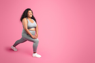 Black plus size woman training, stretching legs and making lunges, pink background, free space, full length