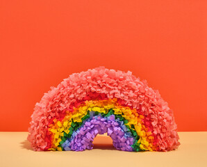 Bright colorful rainbow pinata stands on orange background. Space for text. Atmosphere of holiday energy and lightness.