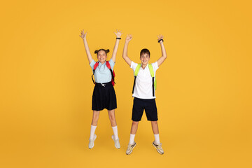 Fototapeta na wymiar Cheerful caucasian teenager girl and boy pupils with backpacks jumping, freeze in air, celebrating victory