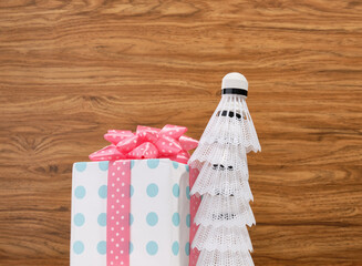 White badminton shuttlecocks and beautiful festive gift box on a wooden background.