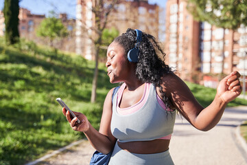 curvy young african american woman walking with wireless headphones listening to music and dancing