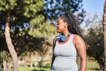 Plus sized African American woman using mobile phone and earphones during the walking at the park in a summer day