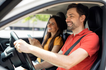 Fototapeta na wymiar smiling millennial couple sitting inside luxury car, woman holding smartphone