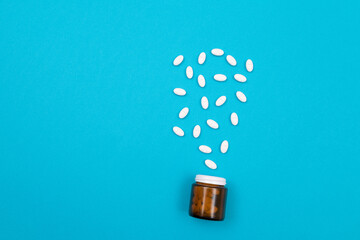 Global Pharmaceutical Industry and Medicinal Products - White Pills or Tablets Scattered from the Pill Container, Lying on Blue Background