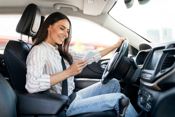 Positive young woman driver using smartphone while driving car