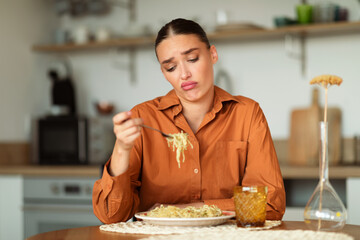 Sad upset young european woman sitting at table in kitchen interior, looking at delivered pasta and dont want to eat it
