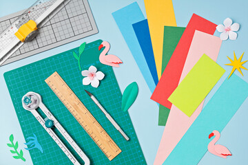 Top view over paper  cut tools, scissors, cutter, cutting mat, and crafted paper objects. DIY...