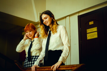 Two uniformed female students standing on a university staircase, laughing joyfully together....