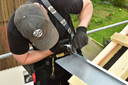 Montage des Traufblechs durch den Dachdecker am Trauf des Steildachs eines Holzhauses durch den Dachdecker