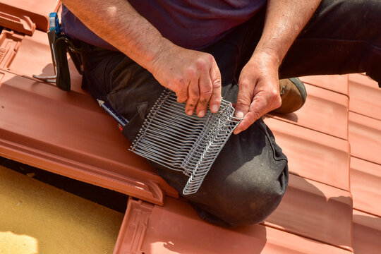 Der Dachdecker verwendet Seitenfalzklammern oder Sturmklammern, um die äußeren Ziegelreihen des Dachs gegen Sturmschaden zu sichern