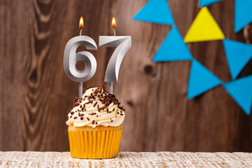 burning candle - birthday number 67 on wooden background with pennants