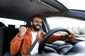 Excited Middle Eastern guy sitting in car gesturing yes - obrazy, fototapety, plakaty