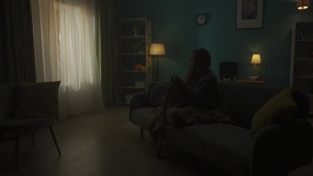 Devastated woman sitting on a sofa in a dark room. A woman desperately thinks about personal problems, is going through a crisis. Change of day and night. Slow motion. HDR BT2020 HLG Material.