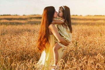 Beautiful young mom and her young daughter cuddling and lounging in a field of wheat at sunset