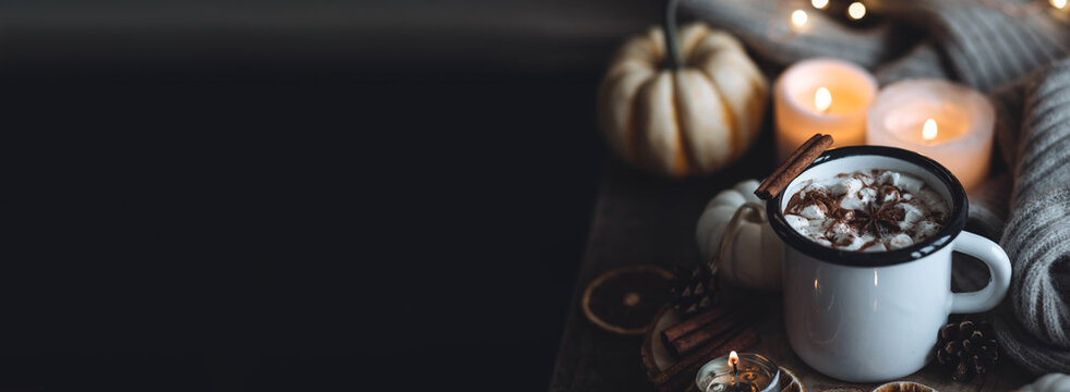 Autumn cozy home composition with hot chocolate with marshmallow and candles. Aromatherapy on a grey fall morning, atmosphere of cosiness and relax. Wooden background close up banner copy space