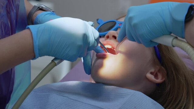 A pediatric dentist performs oral hygiene for a little girl.