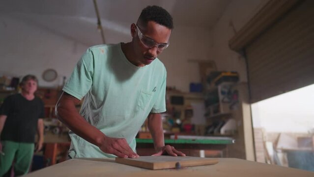 One young black carpenter using machine to trim piece of wood at workshop. Focused employee of carpentry business working meticulously
