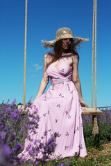 Young beautiful woman sits on a vintage swing in a lavender field against the background of the sky.