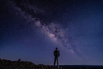 Fototapeta premium Silhouette of Men / boy on the Milky Way. Stargazing at Mauna Loa Observatory Road, Big Island Hawaii. Starry night sky, galaxy astrophotography. 