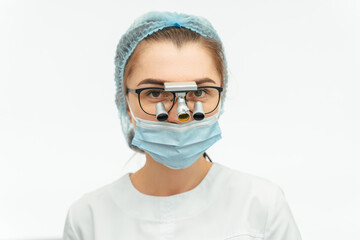 Portrait of female surgeon or dentist in protective mask gloves and cap with dental binoculars